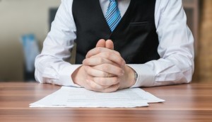 Politician with clapsed hands sitting behind desk.